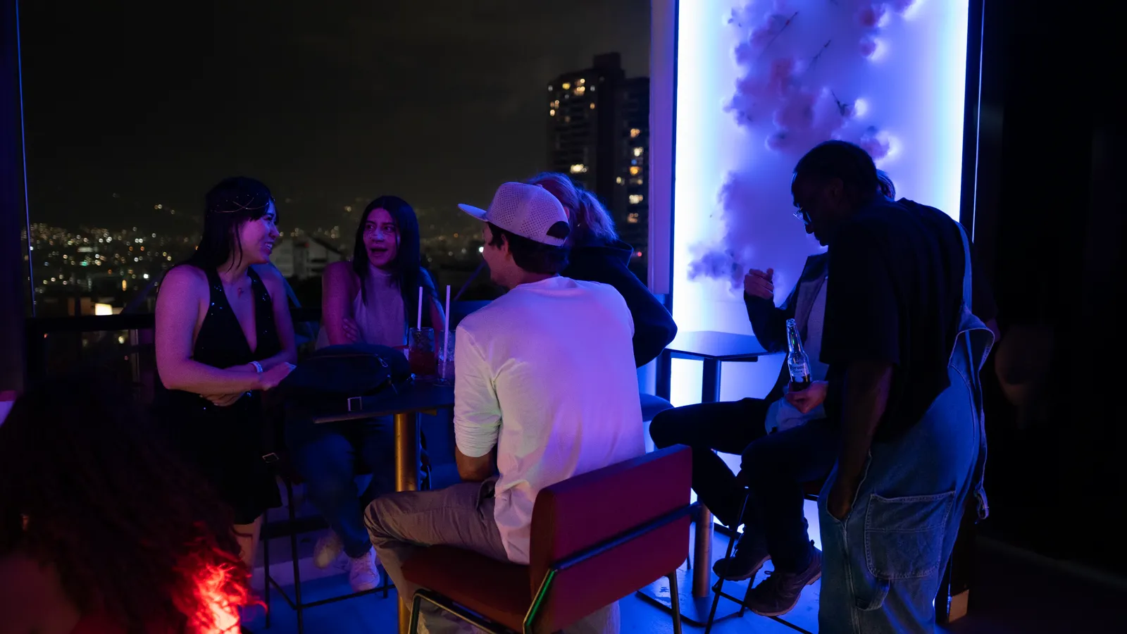 Guests relaxing on a rooftop bar with the city skyline behind them